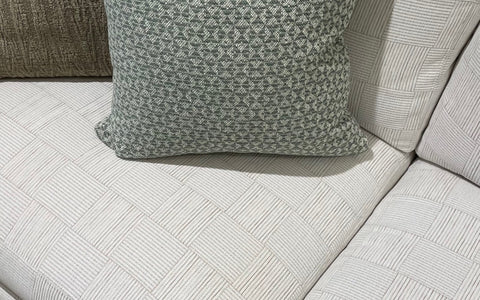 A close-up of the white upholstered sofa with a subtle square pattern, highlighting a textured green throw pillow. The pillow's intricate design contrasts beautifully with the sofa's clean, geometric pattern, emphasizing the refined details of the upholstery.