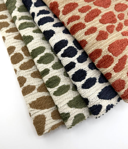 Revolution Performance Fabric swatches arranged in a fanned layout, featuring the Winging It pattern in multiple colorways including jute brown, thyme green, navy blue, and persimmon orange, woven with an abstract scattered motif across an ivory textured ground in a durable, high-performance upholstery fabric suitable for indoor and outdoor use.
