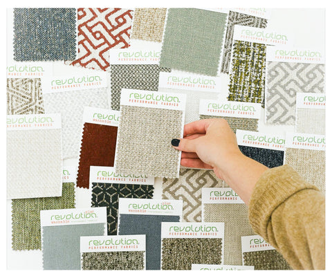 A selection of Revolution Performance Fabrics upholstery swatches displayed in various colors and textures, held by a hand showing options for furniture upholstery.