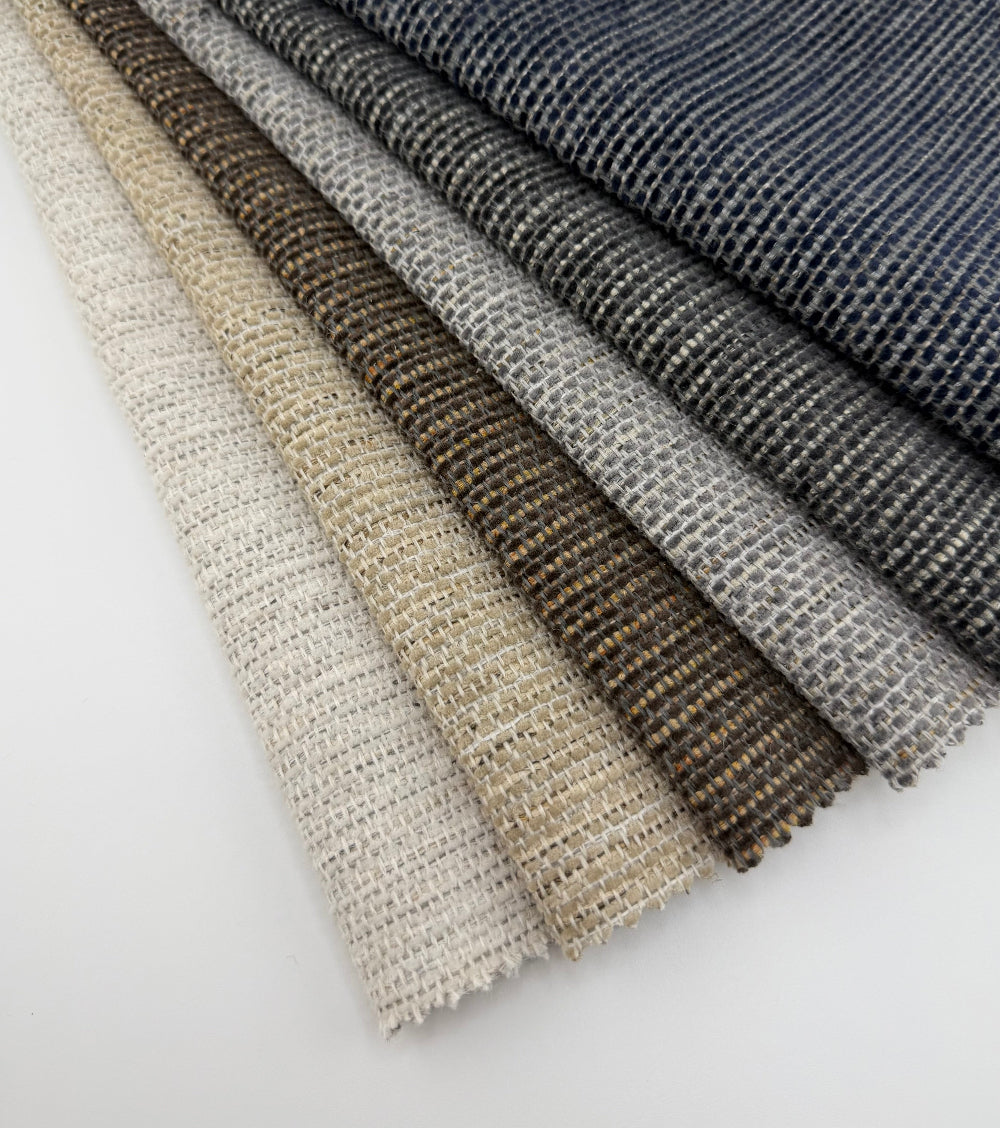 Assorted Revolution Performance Upholstery Fabric swatches from the Whisper collection arranged in a fanned layout. Each swatch displays Whisper’s dense woven texture with fine vertical striation and subtle tonal variation across neutral and deep colorways.